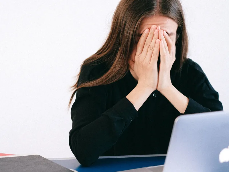 Mulher cobrindo o rosto com as mãos em frente ao notebook, representando estresse